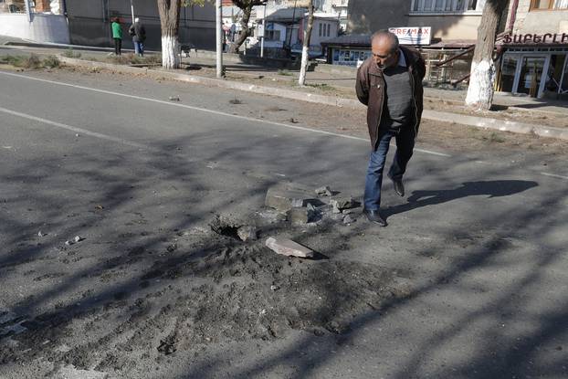 A man looks at a crater in a road surface following recent shelling during a military conflict over the breakaway region of Nagorno-Karabakh, in Stepanakert