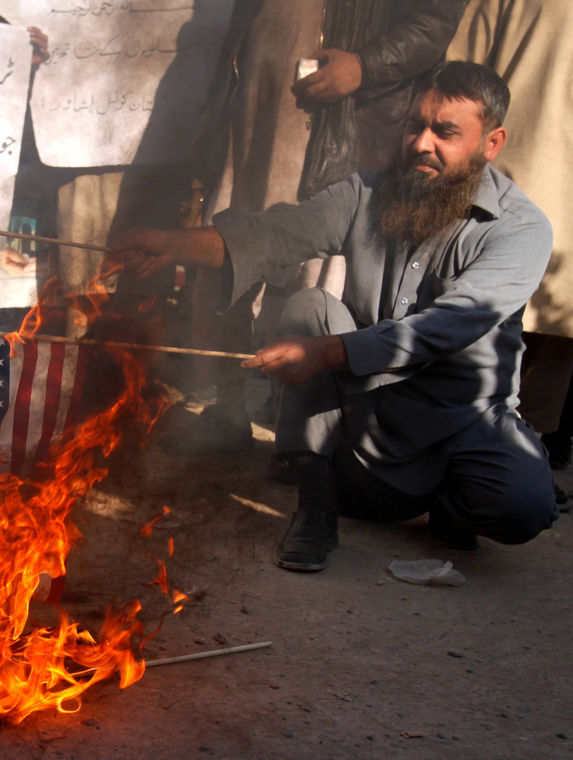 A supporter of the Difa-e-Pakistan Council burns US flags during a protest against U.S. President Trump's decision to recognize Jerusalem as the capital of Israel, in Peshawar