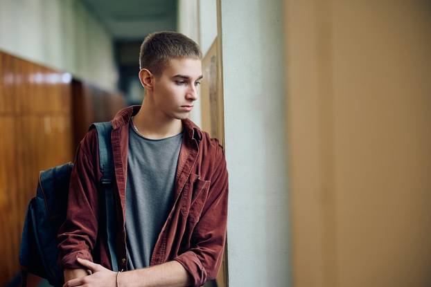 Sad,Teenage,Boy,Standing,Alone,In,Hallway,At,High,School