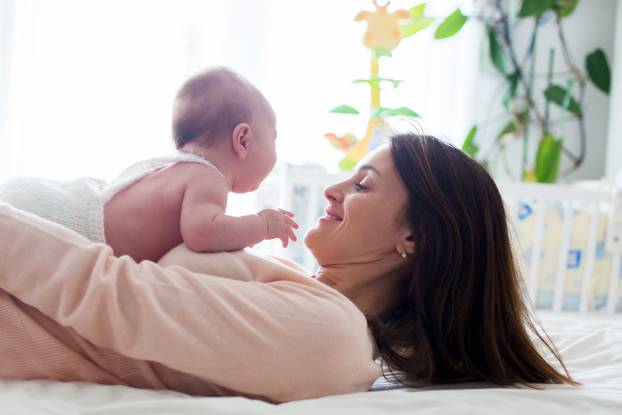 Young mother, caressing her newborn baby boy, holding him in her