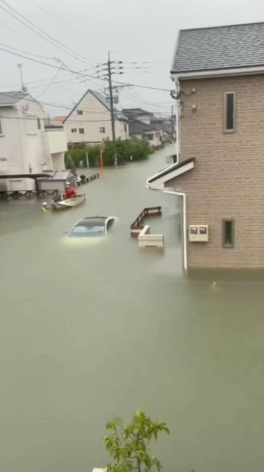 Rescue workers move past a partially submerged vehicle on a flooded street in Kurume