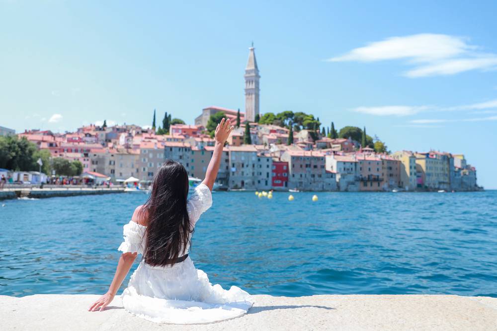 Young,Tourist,Woman,Sitting,On,Harbour,Holding,Her,Hand,Up