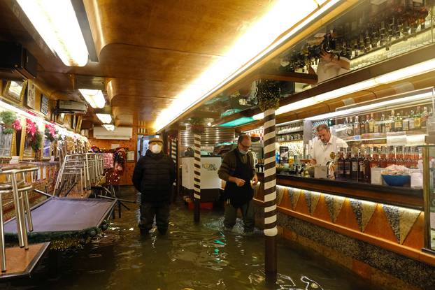 People stand inside a flooded cafe during high tide as the flood barriers known as Mose are not raised, in Venice