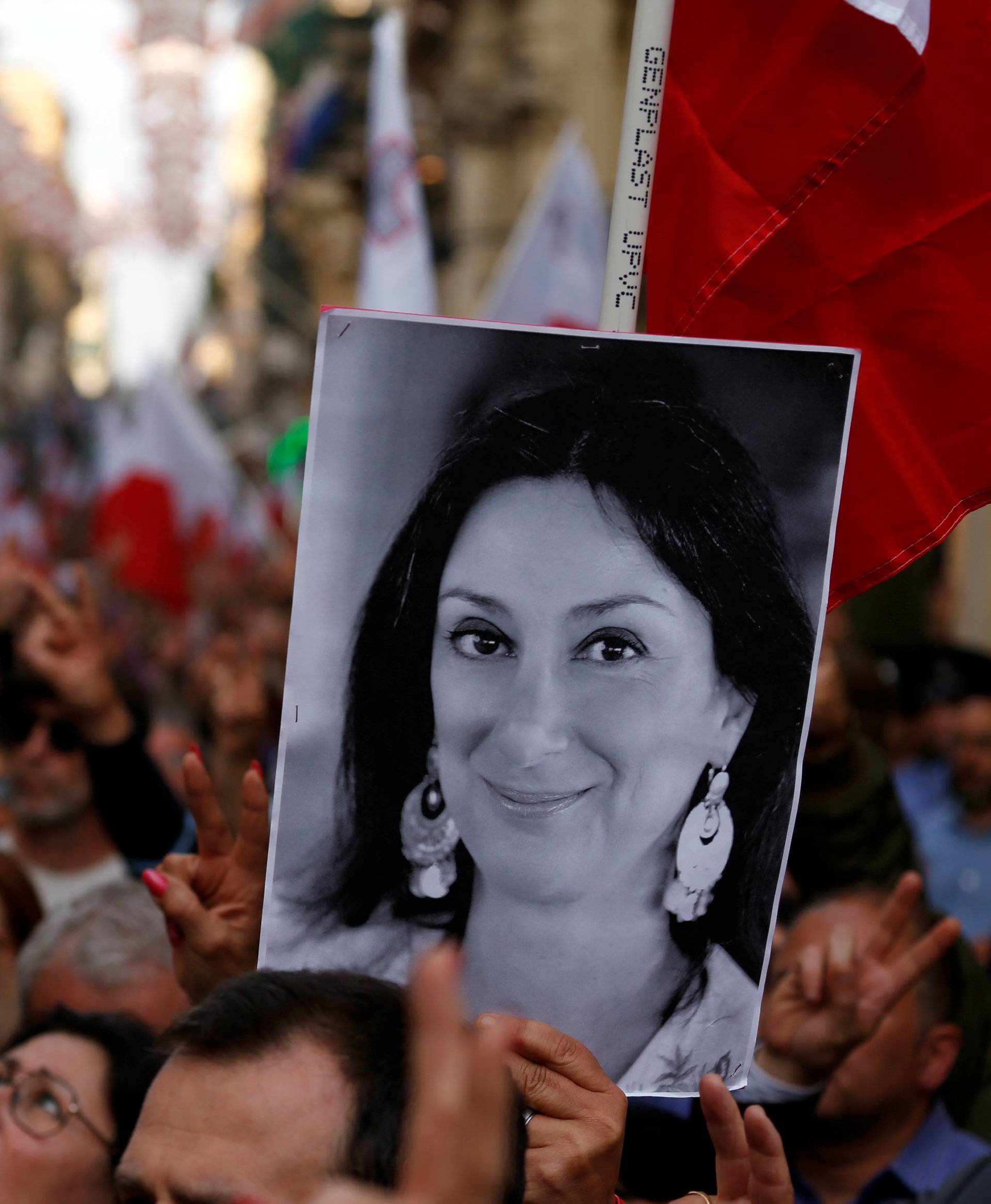 A demonstrator carries a photo of assassinated anti-corruption journalist Daphne Caruana Galizia as others sing the national anthem at the end of a protest against government corruption revealed by the Daphne Project, in Valletta