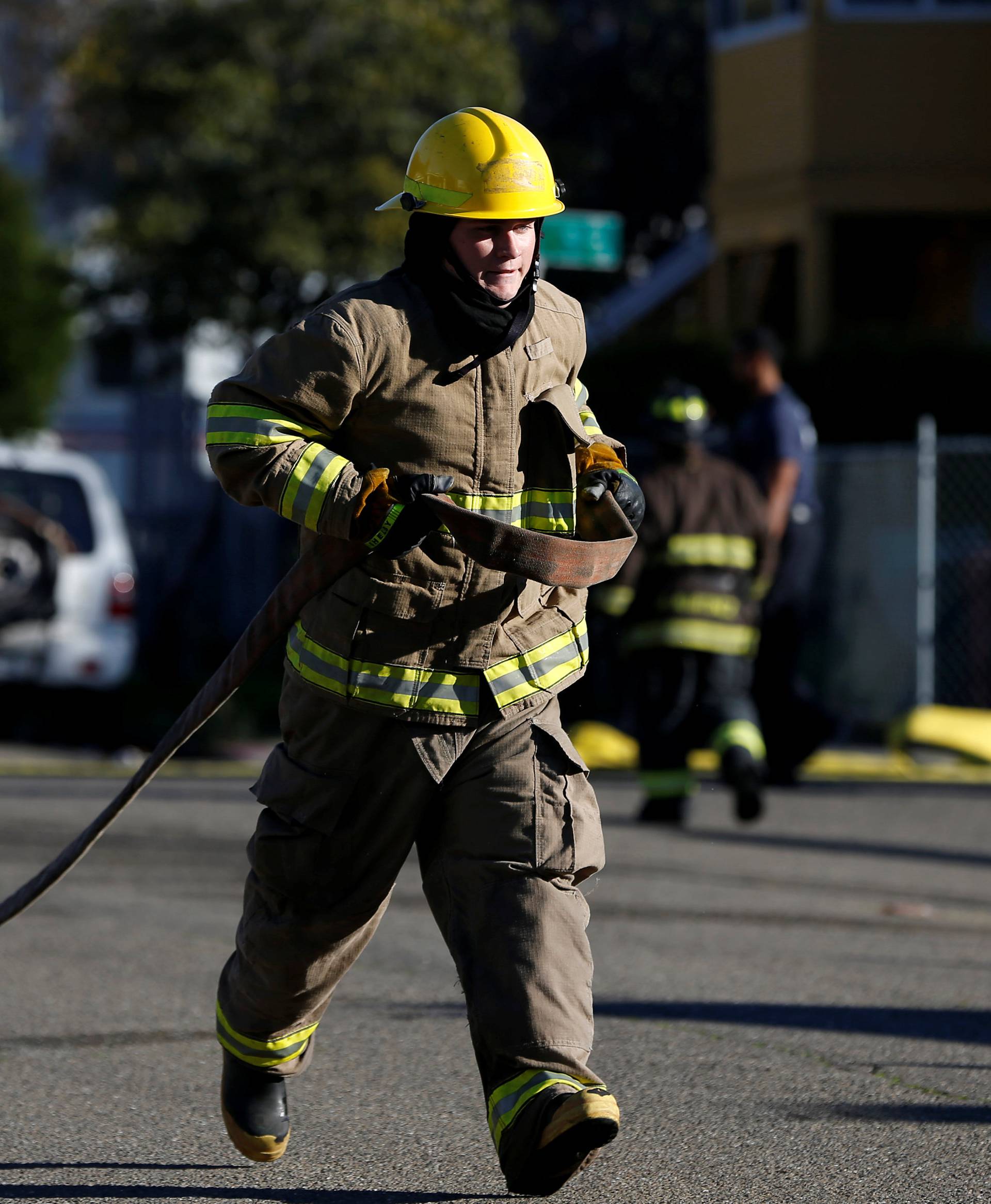 A firefighter carries a water hose near a warehouse where a fire broke out during an electronic dance party late Friday evening, resulting in at least nine deaths and many unaccounted for in the Fruitvale district of Oakland