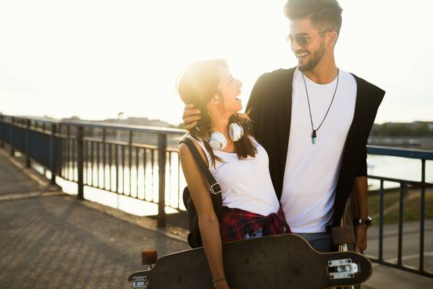 Picture of young attractive couple carrying skateboards