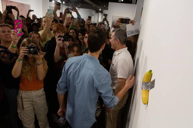 Art Basel visitors use their phones in front of a banana attached with duct-tape that replaces the artwork 