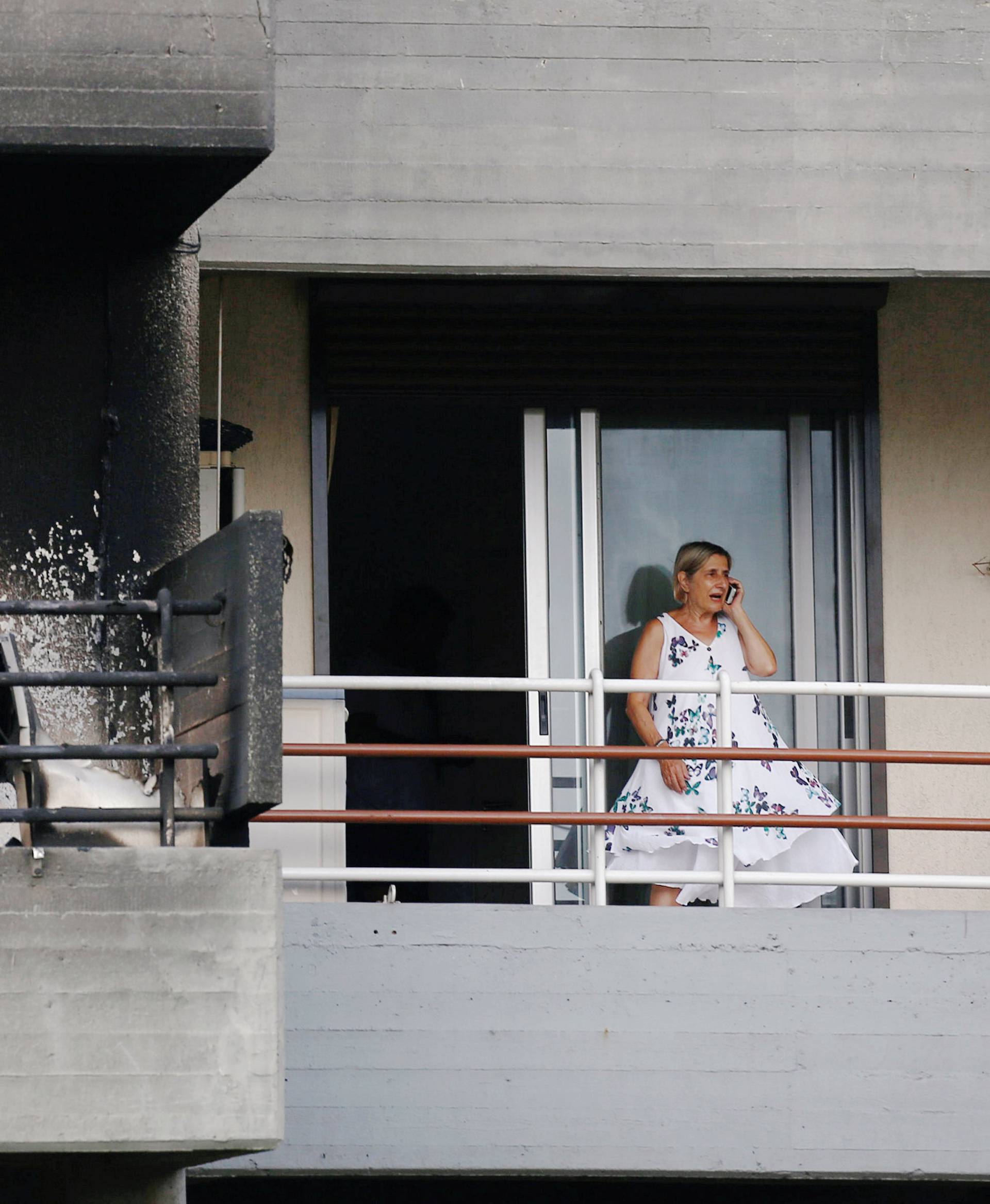 A woman speaks on the phone as she stands next to a burned apartment, following a wildfire at the village of Mati, near Athens