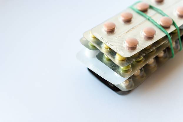 Medicine and pills. Multi-colored medicines on a white background close-up. A pack of plates with multi-colored tablets on a white background fastened with an elastic band. Multi-colored tablets that spilled from an inverted jar onto a white surface.