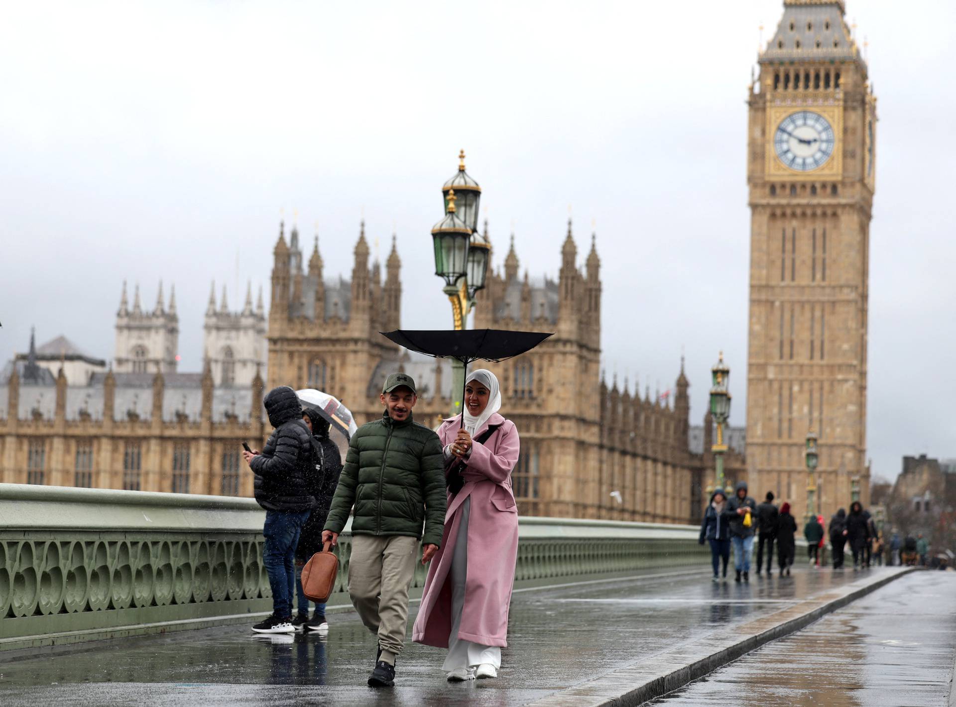 Pedestrians carrying an umbrella cross Westminster Bridge
