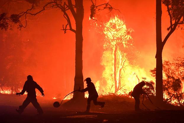 Rural Fire Service (RFS) volunteers and NSW Fire and Rescue officers fight a bushfire encroaching on properties near Termeil