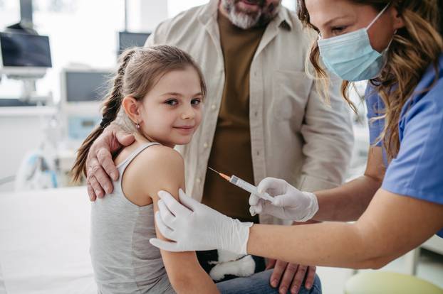 Routine vaccinations for a child. Father holding small girl while pediatrician injecting vaccine in her arm.