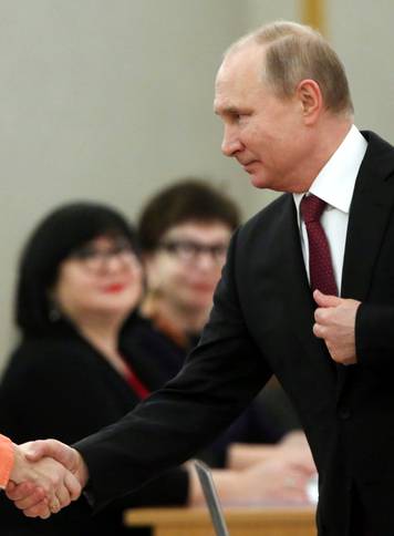 Russian President and Presidential candidate Vladimir Putin shakes hands with a member of a local election commission at a polling station during the presidential election in Moscow
