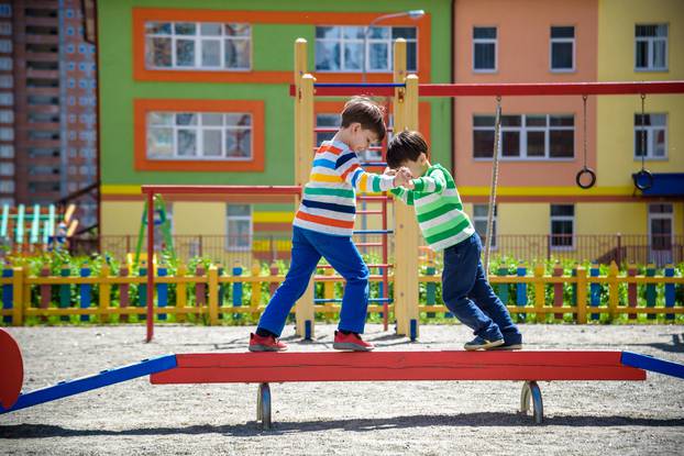 Two little school and preschool kids boys playing on playground outdoors together. children having competition standing on log with outdoor activities in summer sunny day