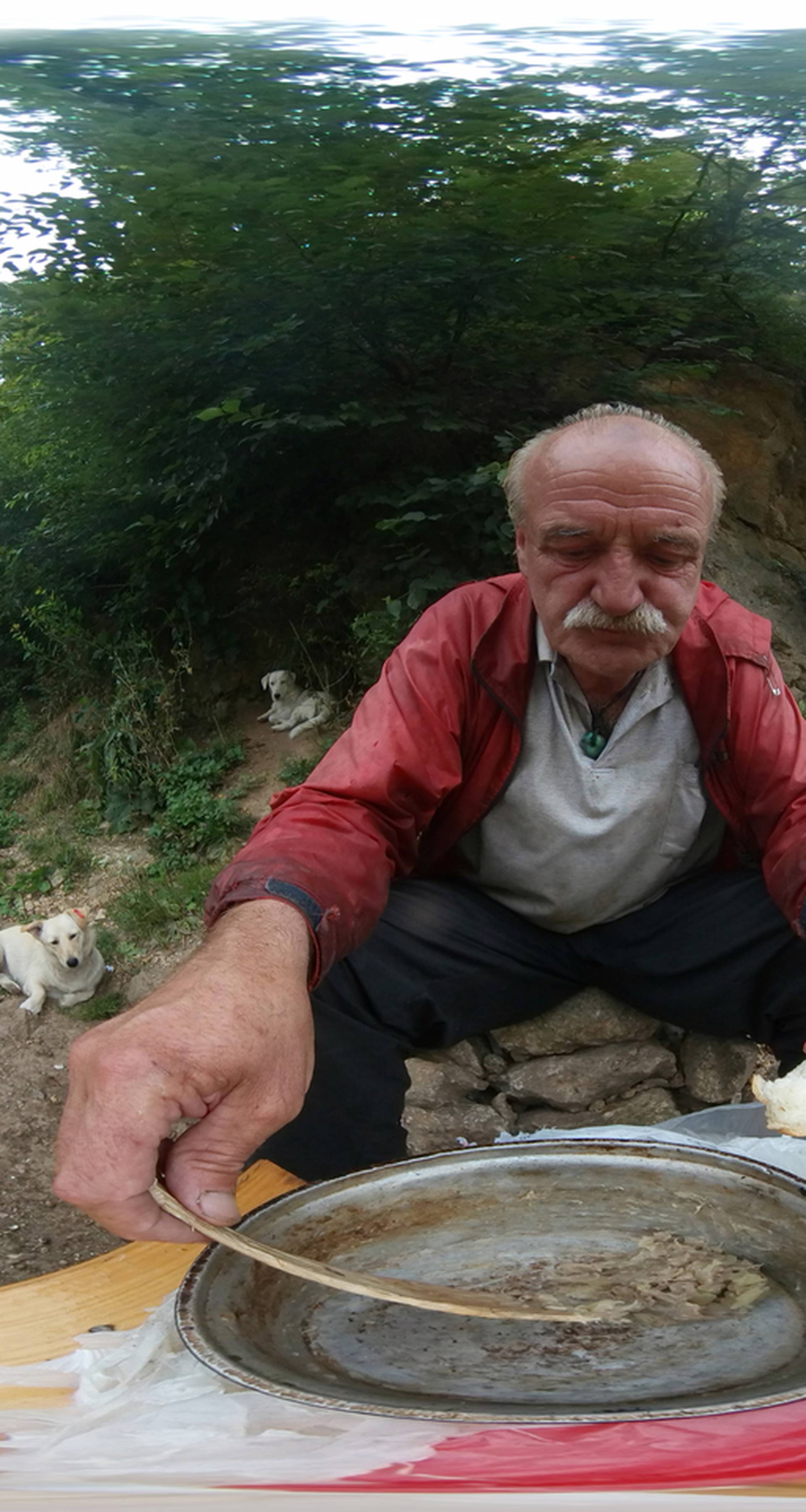 Pieces of bread lie scattered in the dirt as stray dogs watch former steel factory worker Zarko Hrgic scrape the bottom of his food bowl outside his cave