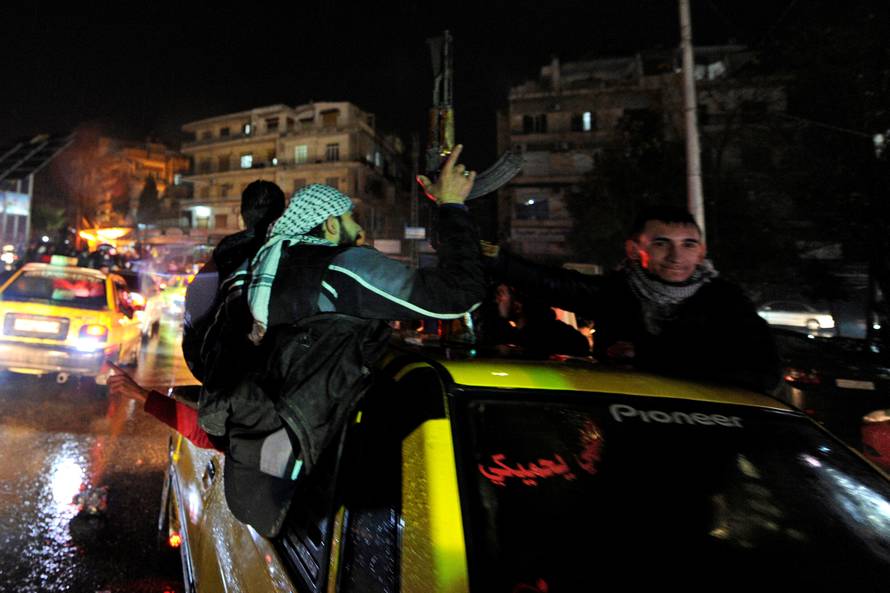 A man holds a weapon while touring with others the streets as they celebrate what they say is the Syrian army's victory against the rebels, in Aleppo
