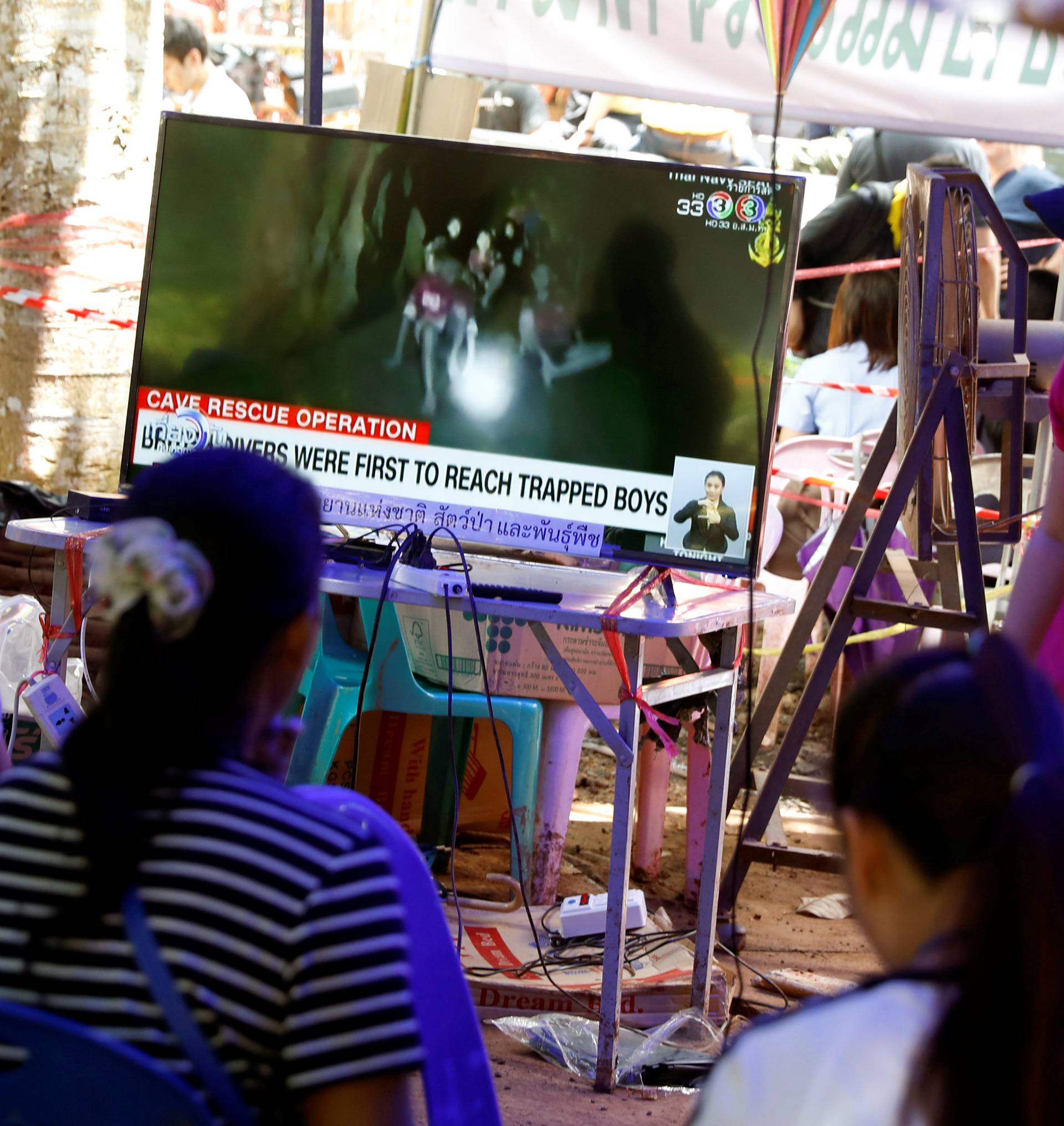 Family members watch a television news broadcast of the trapped members of an under-16 soccer team and their coach, after they have been reported by local media to be found alive, in Chiang Rai