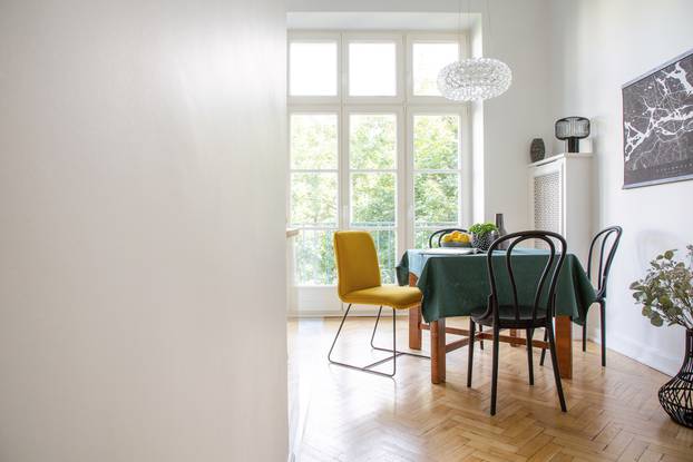 Table with dark green tablecloth, magazine, fresh lemons and plant in real photo of white dining room interior with herringbone parquet, glass lamp and balcony. Empty wall with place for your graphic