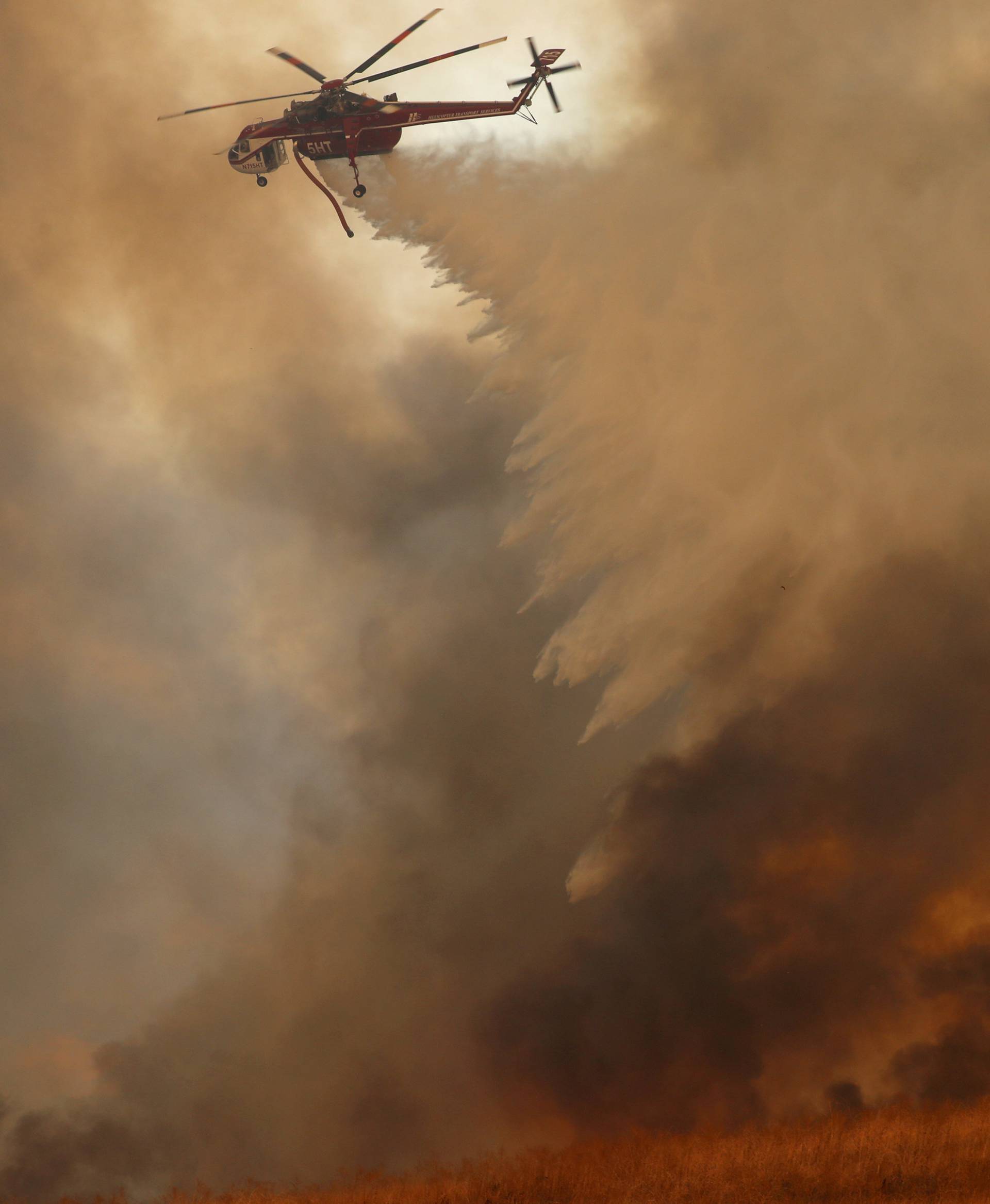 A helicopter drops water on a wind driven wildfire in Orange, California