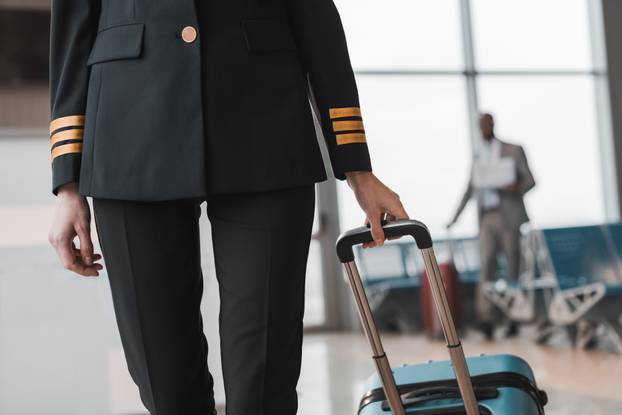 cropped shot of female pilot with suitcase walking by airport lobby