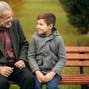 Grandpa and his grandson spend time together in the park. They are sitting on the bench and look to each other