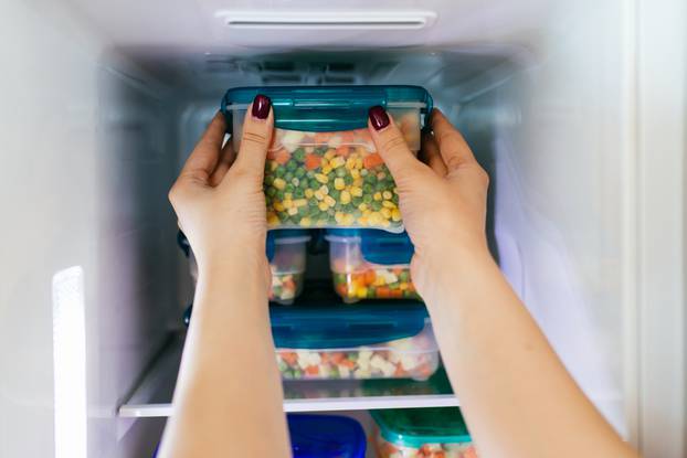 Woman,Placing,Container,With,Frozen,Mixed,Vegetables,In,Freezer.