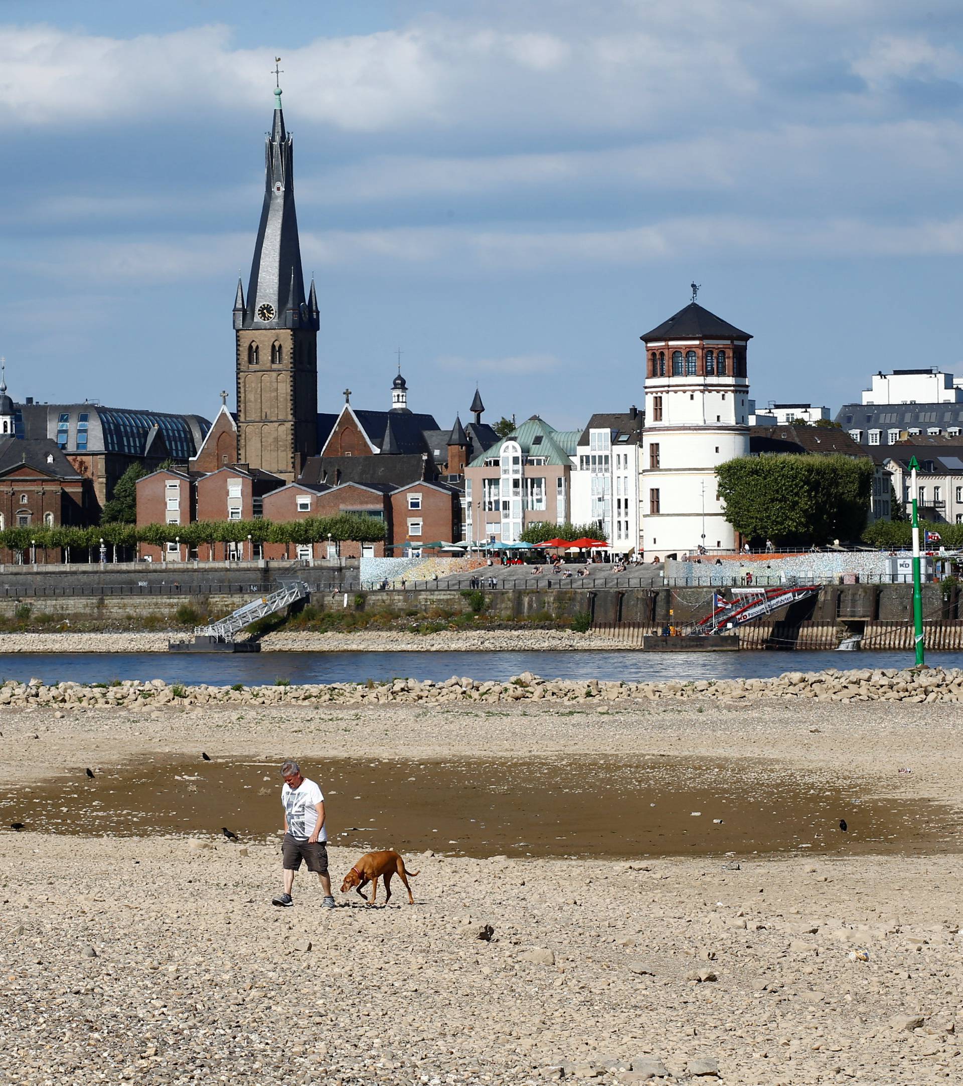 A family walks through the partially dried riverbed of Europe's most important waterway, Rhine in front of the skyline of Dusseldorf