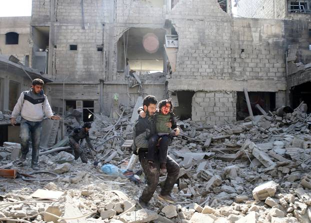 A man carries an injured boy as he walks on rubble of damaged buildings in the rebel held besieged town of Hamouriyeh