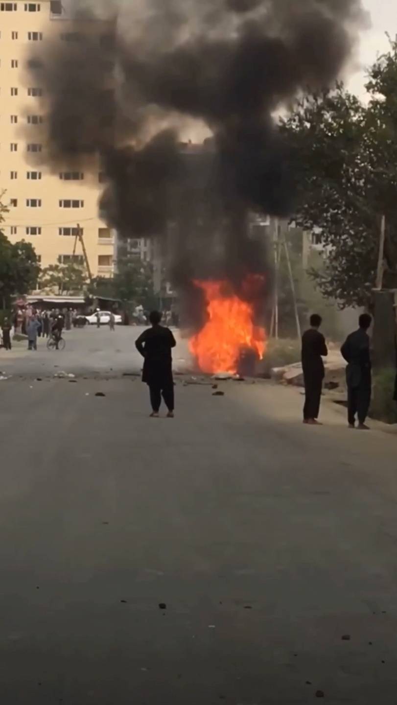 People gather around remnants of flames from cars where rockets towards Kabul's international airport were fired from but were intercepted by a missile defense system in Kabul