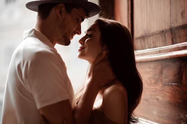 Shot of beautiful female and male in hat, going to kiss each other, express great love and real mutual relationships. Couple in love have passionate kiss, embrace, stand outdoor in darkness