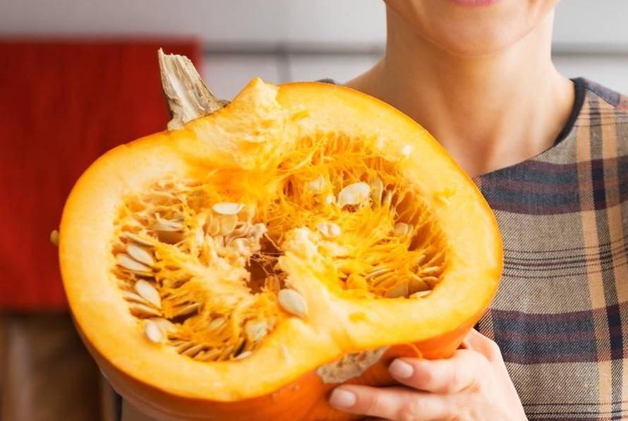 Portrait of happy young housewife showing half of pumpkin