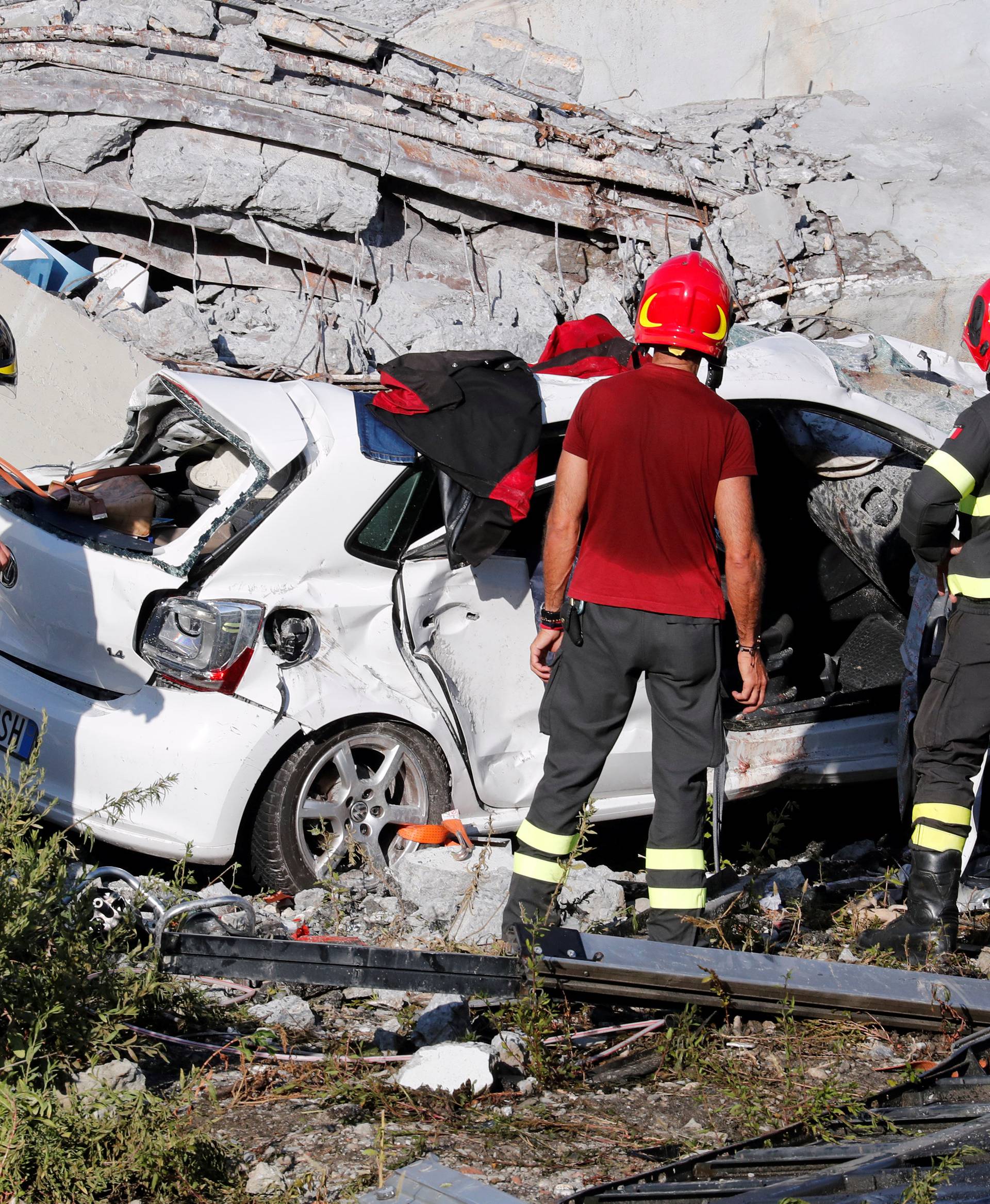 Firefighters stand inspect crushed car at collapsed Morandi Bridge site in Genoa