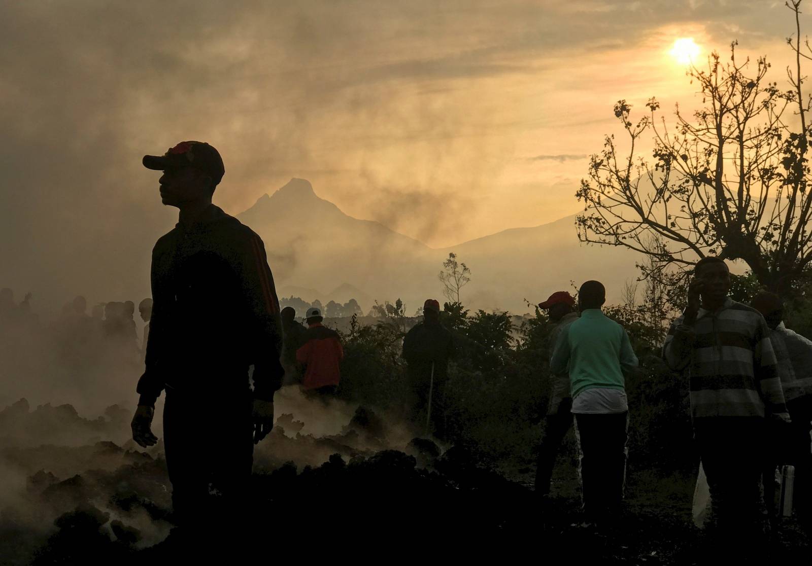Residents walk near destroyed homes with the smouldering lava deposited by the eruption of Mount Nyiragongo volcano near Goma