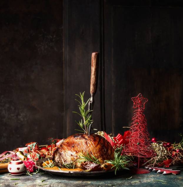 Christmas ham with stuck fork and rosemary on table with festive