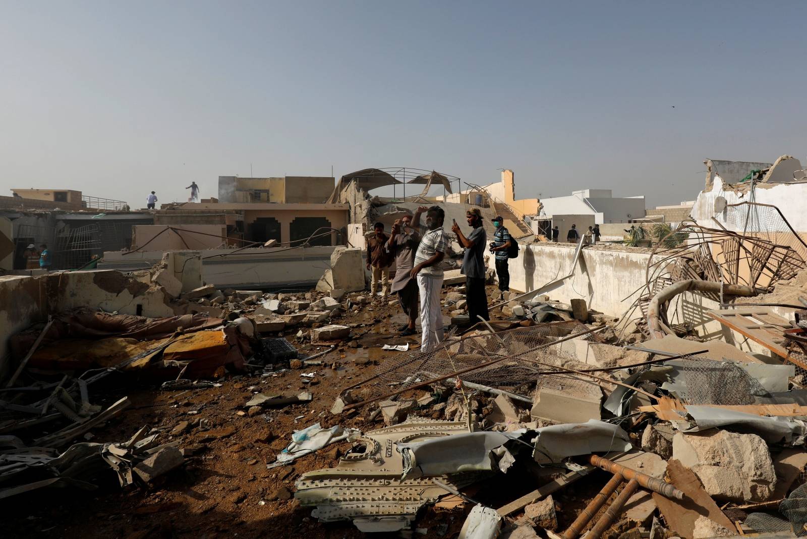 People stand on a roof of a house amidst debris of a passenger plane, crashed in a residential area near an airport in Karachi