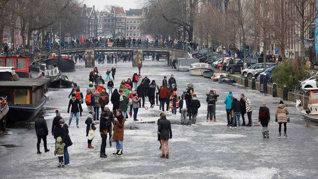 Ice skaters skate and walk on the frozen Prinsengracht canal during icy weather in Amsterdam