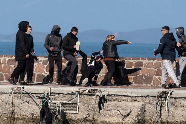 Locals who prevent migrants on a dinghy from disembarking at the port of Thermi beat a journalist, as a woman tries to stop them, on the island of Lesbos, Greece