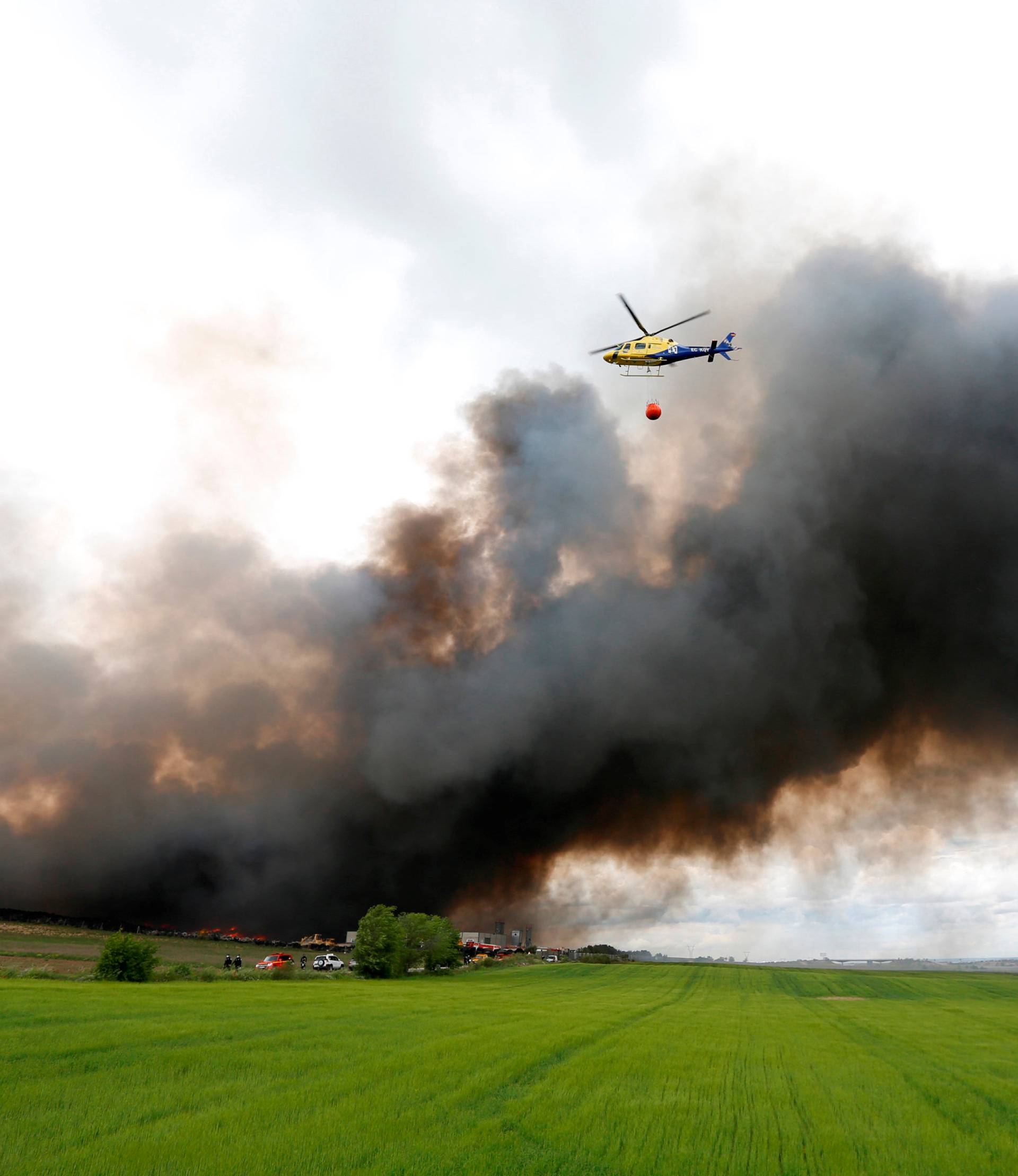 An helicopter prepares to throw water over a fire at a tire dump near a residential development in Sesena
