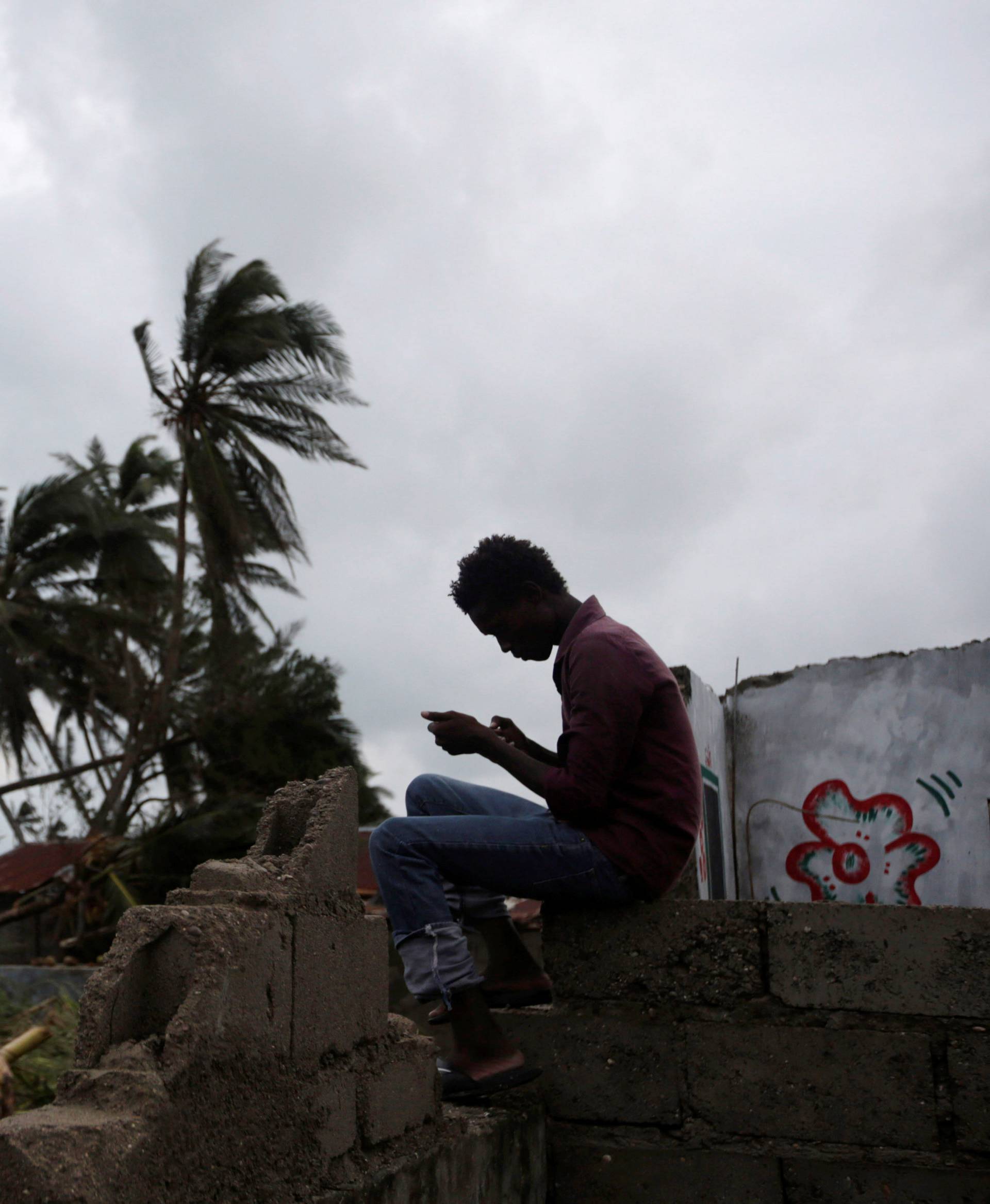 A man checks his phone as he is sitting on the remains of a house destroyed by Hurricane Matthew in Les Cayes, Haiti