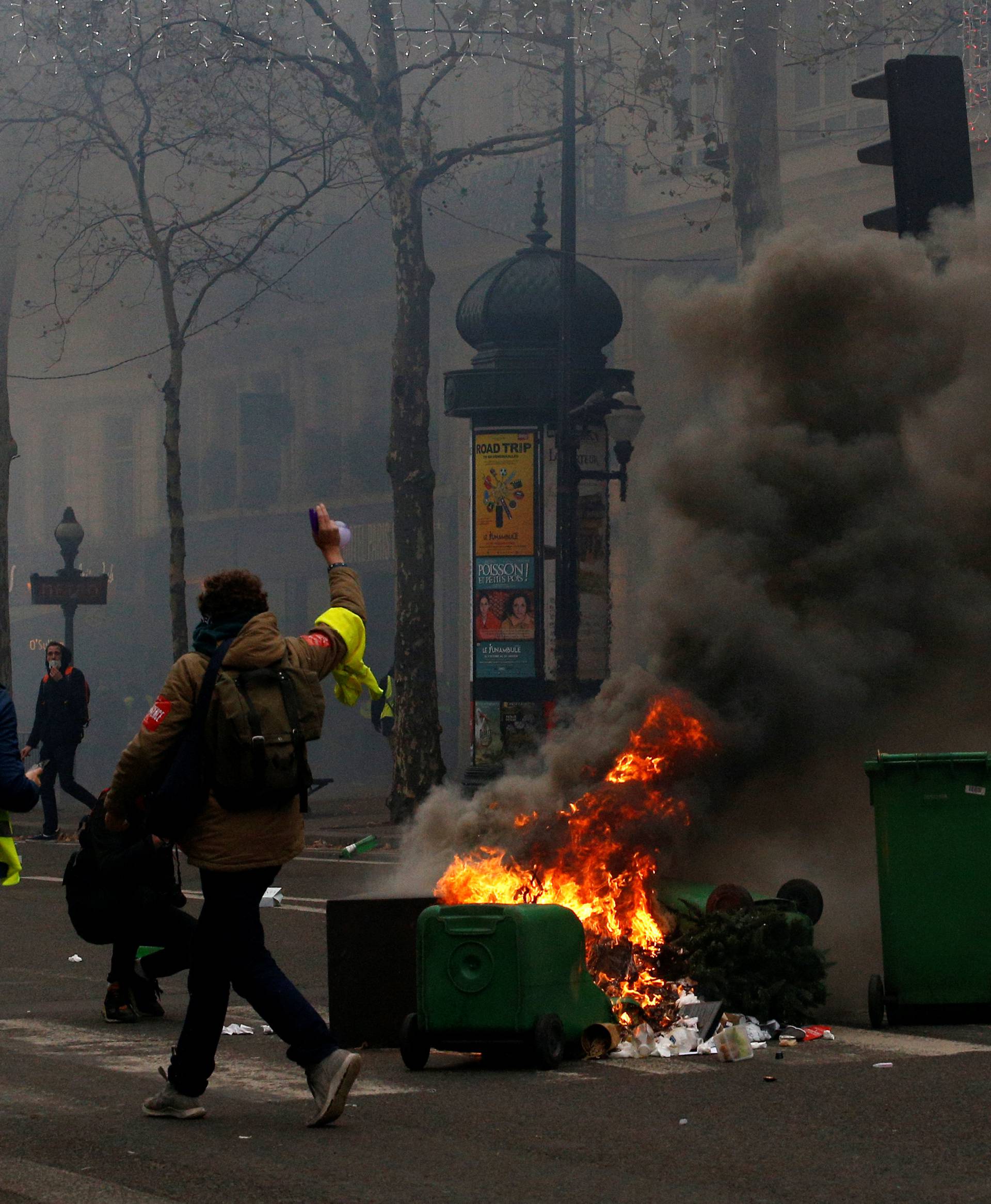 Protesters wearing yellow vests walk past burning trash bins during clashes with police at a demonstration during a national day of protest by the "yellow vests" movement in Paris