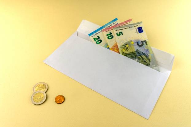A few Euro bills are in an envelope. Also three Euro coins lie on a yellow background.