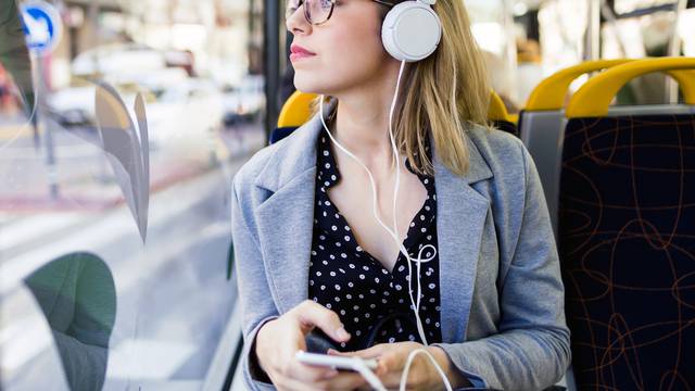 Pretty young woman listening to music with mobile phone at the bus.