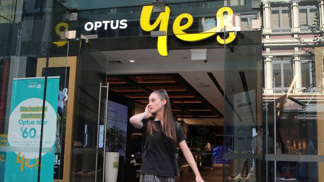 FILE PHOTO: A woman uses her mobile phone as she walks past in front of an Optus shop in Sydney