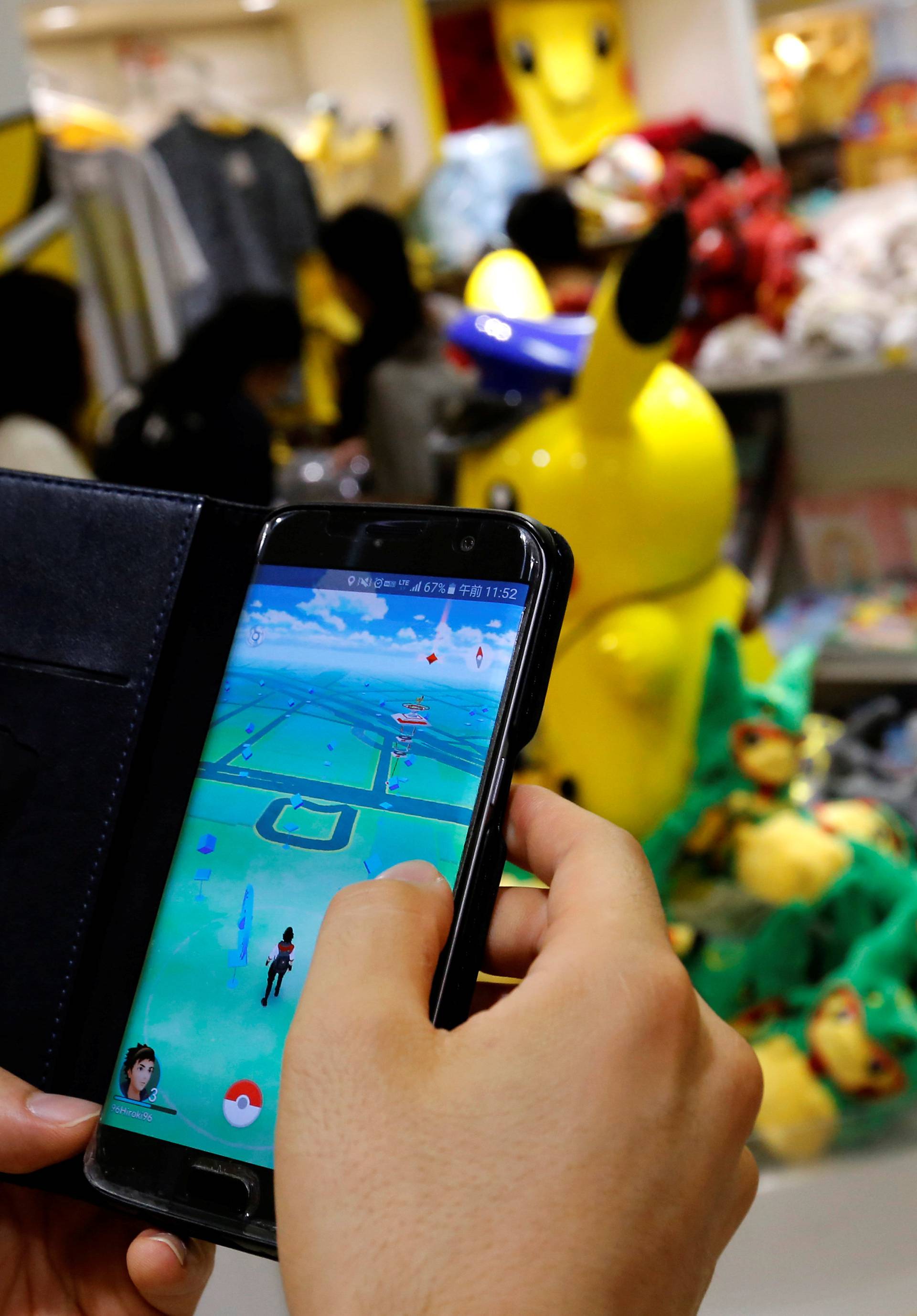 A man plays the augmented reality mobile game "Pokemon Go" by Nintendo in front of a shop selling Pokemon goods in Tokyo
