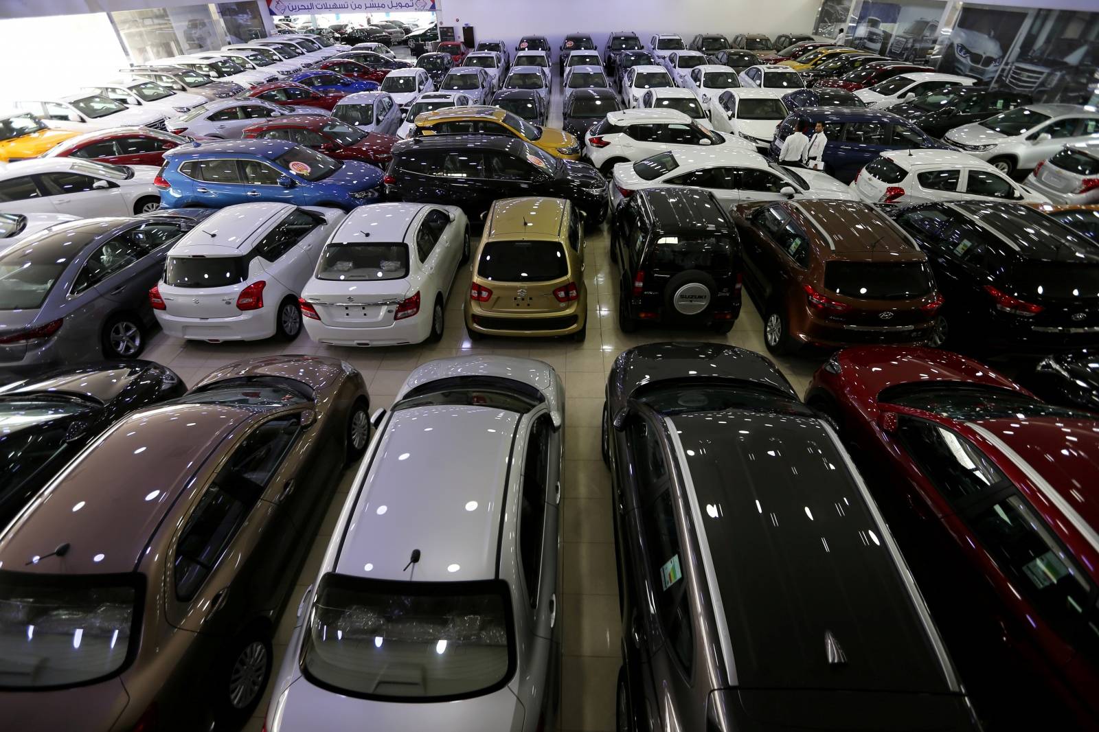 FILE PHOTO: Auto dealers stand between cars displayed for sale at a second hand showroom outside Manama, Bahrain