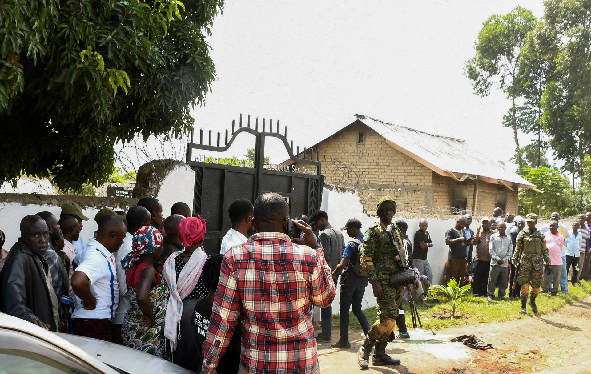 FILE PHOTO: Ugandan security forces stand guard as locals gather at the cordoned scene outside the Mpondwe Lhubirira Secondary School