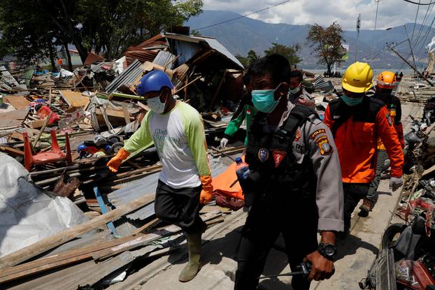 Rescue team members carry a dead body as they walk among ruins after the earthquake in Palu