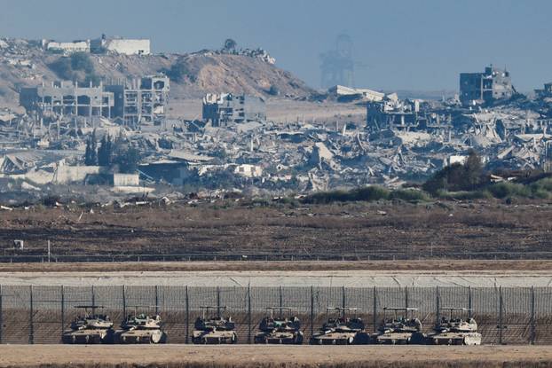 Tanks stand on the Israeli side of the border, as destruction in Gaza is seen in the background
