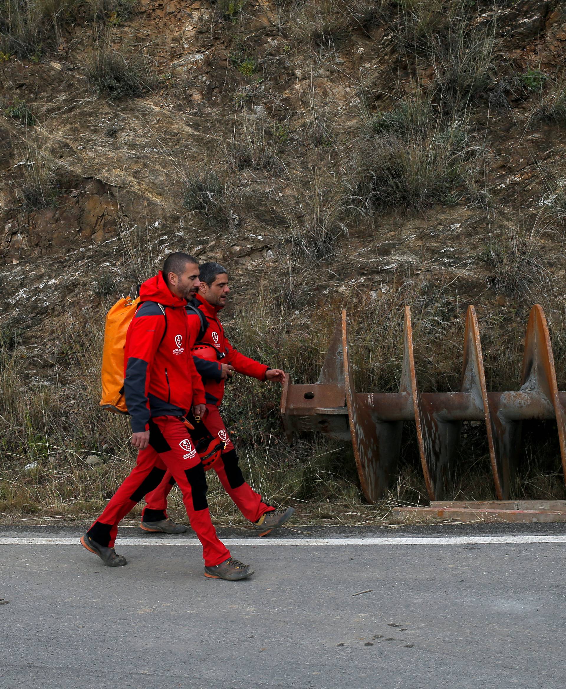 Mountain rescue firefighters walk past a piece of a drill on a road in Totalan