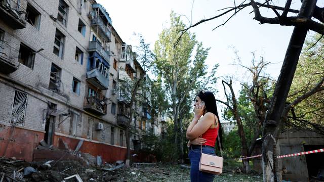 A Ukrainian woman uses her mobile phone in front of a residential building damaged after a Russian strike, as Russia's attack on Ukraine continues, in Kramatorsk